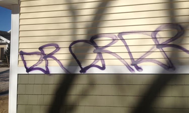 Purple graffiti across cream residential siding before removal